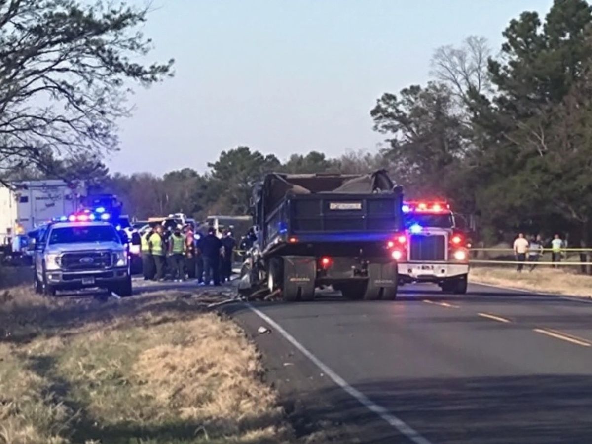 Dump truck on rural road with emergency vehicles nearby.